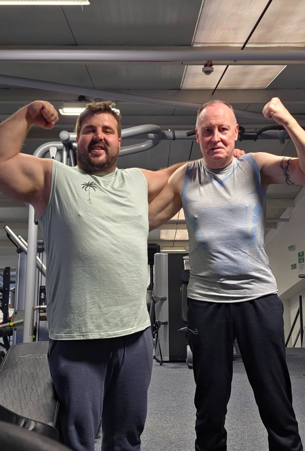 Kurt with a client, both flexing their arms in the gym